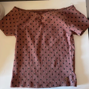 Brun prickig offshoulder topp Ü - Säljer en rosa offshoulder topp från Ü med svarta prickar. Toppen har korta ärmar och är gjord i ett skönt, lätt rynkat bomullstyg. 
