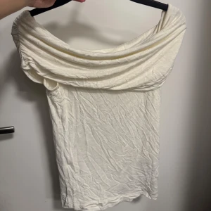 Vit offshoulder topp - Oanvänd! Snygg offshoulder-design och draperad krage. Toppen är ärmlös och har en mjuk, lätt struktur i bomullsmaterial. Perfekt för dig som gillar stilrena och enkla plagg med en twist.