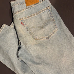 Levis 502 ljusblå jeans straight fit - Ljusblå Levis 502 jeans med klassisk femficksdesign och brunt läderpatch bak i midjan. Jeansen har raka ben och normal passform, tillverkade i mjukt denimtyg. Perfekta för en avslappnad och stilren look. Jag är 173cm o väger 70 passar perfekt. Längd 30 midja 32
