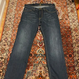 Mörkblå jeans från Lee W31 L32 - Säljer ett par mörkblå jeans från Lee med klassisk femficksdesign och snygga kontrastsömmar. Jeansen har rak passform och är tillverkade i slitstarkt denimtyg. Perfekta för dig som gillar en tidlös och clean look. 