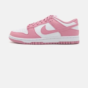 Nike Dunk Low rosa och vita sneakers - Nike Dunk Low sneakers i en snygg rosa och vit färgkombination. Skorna har klassisk låg siluett, snörning och perforerad tåbox. Tillverkade i skinn med mjuk textil på insidan och slitstark yttersula. Perfekta för dig som vill sticka ut med stilrena sneakers.