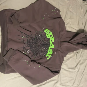 Grå hoodie Spider med spindelnätsprint - Pris kan diskuteras. Säljer en grå hoodie från Spider i storlek M. Tröjan har ett stort svart spindelnätsmönster och neongrön text på framsidan, samt små stjärnor i grönt och vitt på ärmarna. Tillverkad i 100% bomull och har en klassisk huva. Perfekt för dig som gillar coola tryck och streetwear.