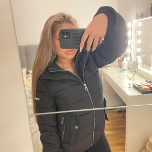 Svart pufferjacka  - Säljer en svart pufferjacka. Jackan har två fickor med dragkedja och en knapp, samt diskret logga på ärmen. Säljer tyvärr eftersom den aldrig har kommit till användning. Storlek S passar även Xs