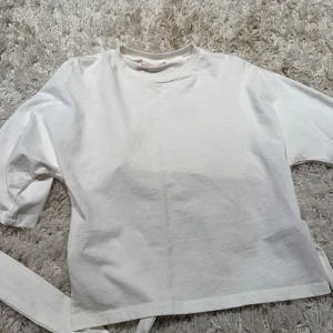 Vit omlottopp med knyt från Nelly - Säljer en vit omlottopp från Nelly i storlek XS. Toppen har långa ärmar, rund halsringning och knytband i midjan som ger en snygg omlotteffekt baktill. Tillverkad i mjuk bomull för en skön känsla och clean look.
