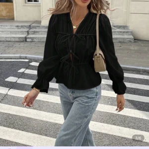 Svart blus med knyt och puffärm - Svart blus med v-ringning, knyt framtill och långa puffärmar. Blusen har en lös passform och är perfekt för dig som gillar trendiga detaljer. Snygg att styla med jeans eller kjol.