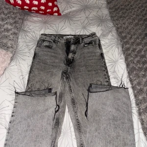 Grå jeans med råa kanter från Zara - Säljer ett par grå jeans från Zara med cool tvättad look och råa, avklippta kanter vid knäna. Modellen har fem fickor, bälteshällor och klassisk knappstängning. Passar dig som gillar edgy streetstyle och vill sticka ut.