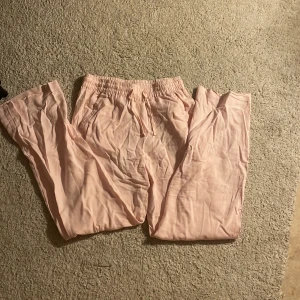 Ljusrosa linnebyxor från 157 - Säljer ett par ljusrosa linnebyxor från 157 med resår och snörning i midjan. Byxorna har raka ben och är tillverkade i ett tunt, svalt linnematerial. Perfekta för en chill och avslappnad stil. Har aldrig använt lite skrynkliga för har legat i min garderob 