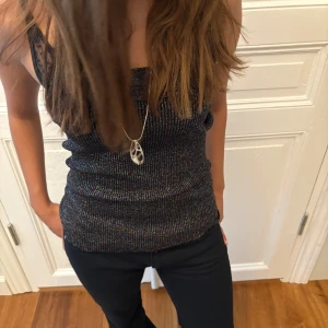 Glittrig svart tubtopp - Säljer en glittrig svart tubtopp med diskret regnbågsskimrande trådar. Toppen är ribbad och sitter tight mot kroppen. Perfekt för dig som vill sticka ut lite extra med en snygg bandeau-modell. Materialet känns stretchigt och bekvämt och kan användas som kjol🤗