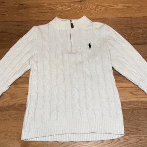 Ralph Lauren Half Zip - Vit kabelstickad tröja från Polo Ralph Lauren med halv dragkedja och klassisk broderad logga på bröstet. Tröjan har ribbade muddar, hög krage och lång ärm. Perfekt för lager-på-lager och snygg till jeans. Hör av er vid några frågor, storlek S/M