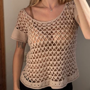 Beige virkad blus med kort ärm - Säljer en beige virkad blus med korta ärmar och rund halsringning. Toppen har ett öppet, nätliknande mönster och är tillverkad i bomull. Perfekt att styla över ett linne eller bikini för en chill look.