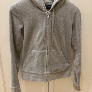 Grått set från Juicy Couture S - Grå mjukisbyxor/hoodie från Juicy Couture i storlek S. Byxorna har raka ben, framfickor och bakfickor med knappdetalj. Dem är lite slitna längst ner, då dom vart för långa på mig.Tillverkade i mjukt material som är perfekt för en chill look. Klassisk Juicy Couture-stil med diskret logga.