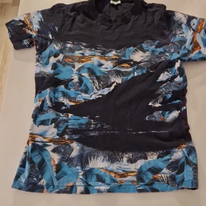 Kenzo blå mönstrad t-shirt L - Snygg t-shirt från Kenzo i storlek L med coolt blått och svart abstrakt mönster och inslag av orange. T-shirten har korta ärmar och är tillverkad i mjuk bomull. Perfekt för dig som vill sticka ut med en unik design.den som köper betalar för frakt även om det ska till ett snat land 