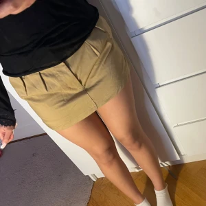 Beige kortkjol med veck - Stilren kort kjol i beige/ khakigrönt med snygga veck framtill. Mjuk och bekväm kvalitet med lite stretch – perfekt både till vardag och fest. Storlek: XS (EUR 34 / US XS) Mycket fint skick, använd få gånger.  🫶 Enkel att matcha med allt – stickad tröja, skjorta eller linne!