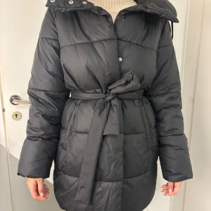 Svart pufferjacka från Vero Moda S - Helt ny Svart pufferjacka från Vero Moda med bälte i midjan och huva. Helt ny och oanvänd med prislapp. Köpt för 950 men säljer för 600