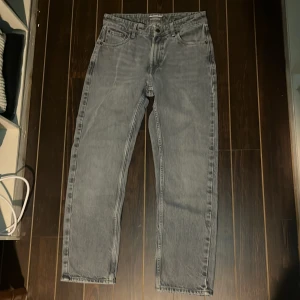 Grå jeans från Dressmann 29/30 - Snygga grå jeans från Dressmann i klassisk rak modell. Jeansen har fem fickor, bälteshällor och en diskret tvättad look. Perfekta för dig som gillar en enkel och stilren vibe. Materialet är tåligt denim i bomull.