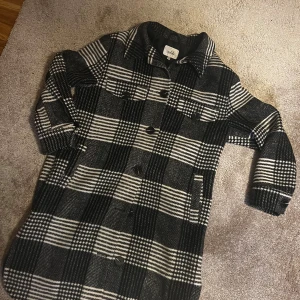 Rutig lång overshirt från Isolde - PRIS KAN DISKUTERAS PRIVAT* Snygg lång overshirt från Isolde i svartvitt rutigt mönster. Jackan har klassisk krage, knäppning framtill med svarta knappar och två bröstfickor. Materialet är mjukt och känns ulligt, perfekt för lager-på-lager under höst och vinter. Aldrig använd