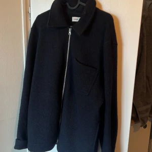 Svart overshirt från Samsoe Samsoe - Stilren svart overshirt från Samsoe Samsoe med rak passform, klassisk krage och bröstficka. Jackan har en grov dragkedja framtill och är tillverkad i mjuk ullblandning. Perfekt för lager-på-lager och enkel att matcha med olika outfits.