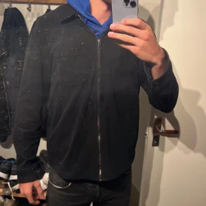 Svart overshirt med dragkedja - Stilren svart overshirt med klassisk krage och bröstficka. Jackan har hel dragkedja framtill och raka ärmar. Perfekt för lager-på-lager och enkel att matcha med det mesta. Materialet känns mjukt och har en matt finish.