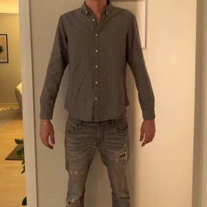 Grå skjorta från Pull&Bear, L - Stilren grå skjorta från Pull&Bear i storlek L. Skjortan har klassisk krage med knappar, långa ärmar och är tillverkad i 100% bomull. Perfekt för dig som gillar en enkel och clean look.