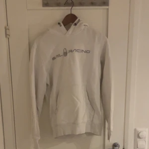  hoodie Sail Racing - Finns inte att köpa ny! Vit hoodie från Sail Racing med logga tryckt på bröstet och snörning i huvan. Tröjan har en klassisk känguruficka framtill och ribbade muddar vid ärmslut och nederkant. Perfekt för dig som gillar stilren och sportig look. SKRIV VID FRÅGOR!!!