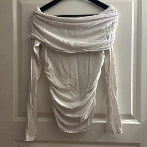 Vit offshoulder topp från Weekday - Säljer en vit offshoulder topp från Weekday i storlek S. Toppen har långa ärmar och snygga rynkade detaljer längs axlarna och sidorna. Materialet är mjukt och stretchigt, perfekt för att skapa en cool och avslappnad look.
