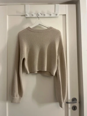 Beige croppad stickad tröja XS - Säljer en beige croppad stickad tröja från Divided i storlek XS. Tröjan har långärmad modell, ribbade muddar och en avslappnad passform. Perfekt till höst och vinter för en chill och snygg look. Knappast använd lite ludd på ena armen