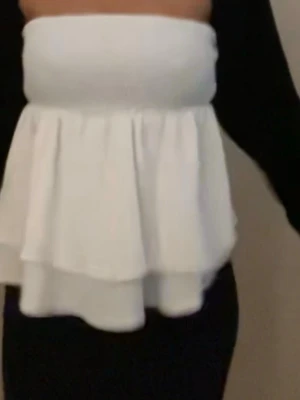 Vit bandeau tubtopp med volanger - Säljer en vit bandeau tubtopp med dubbla lager volanger nedtill. Toppen är axelbandslös och har en smockad, elastisk överdel som sitter bekvämt runt bröstet. 