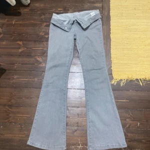 Grå bootcut jeans med låg midja - Säljer ett par ljusgrå jeans med bootcut-modell och låg midja. Byxorna har klassisk femficksdesign och är tillverkade i mjukt denimtyg. Perfekta för dig som gillar retrovibbar och vill ha ett par riktigt snygga jeans med utsvängda ben.