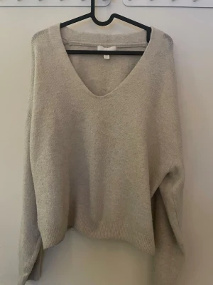 Beige stickad tröja med v-ringning H&M - Mysig beige stickad tröja från H&M i storlek XS. Tröjan har en djup v-ringning och långa ärmar med ribbade muddar vid ärmslut och nederkant. Perfekt för lager-på-lager och chill dagar. Enkel och stilren design som funkar till många outfits.