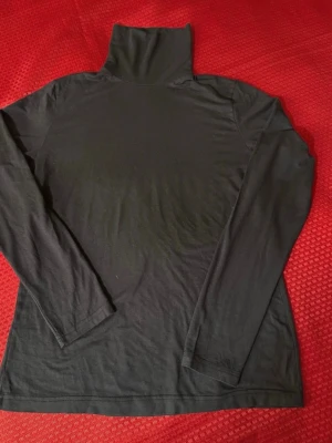 Mörkt grå  polotopp med lång ärm S , 95% viskos, 5% elastan.  - Mörkt grå polotopp  med lång ärm i mjukt och stretchigt material. Enkel och stilren design med hög polokrage och raka sömmar. Perfekt att styla lager på lager eller med jeans. Passformen är normal och toppen är ärmlös. Bredd: 33cm, längd:57cm 