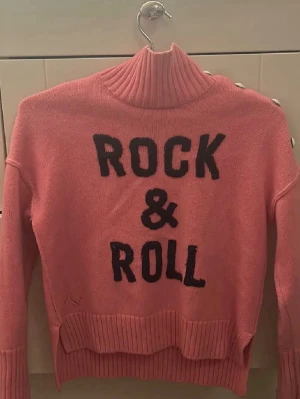 Zadig voltaire tröja🩷🩷🩷 - Cool rosa polotröja med svart text 'ROCK & ROLL' framtill. Tröjan har ribbade muddar och hög polokrage som ger en extra mysig känsla. Perfekt för dig som vill sticka ut med en statement-tröja i garderoben.