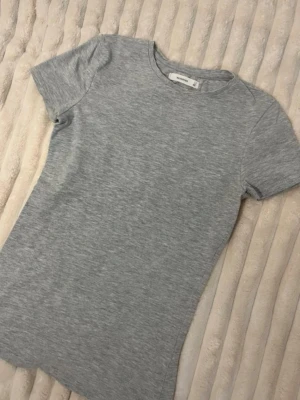 Tajt kortärmad tröja - strl S - Enkel och stilren grå t-shirt från Reserved i storlek S. T-shirten har rund halsringning och korta ärmar, perfekt för en clean och avslappnad look. Tillverkad i mjuk bomull som känns skön mot huden.