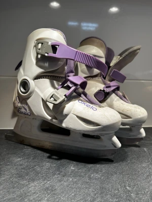 Vita och lila skridskor från Oxelo - Säljer ett par vita och lila skridskor från Oxelo med justerbar storlek (EU 32-34). Skridskorna har två lila spännen för enkel påtagning och en mjuk, fleecefodrad insida för extra komfort. Perfekta för vinterns åk på isen! Behöver slipas!