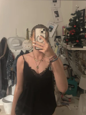 Två linnetoppar med spetsdetaljer - Säljer två linnetoppar med tunna axelband och v-ringning, båda med spetskant längs urringningen och bak . En är svart och den andra är gråblå har andvända 1 gång 