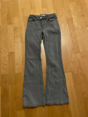 Grå bootcut byxor från Lindex - Snygga grå bootcut-byxor från Lindex med klassisk femficksdesign och knapp med Detroit-logga. Byxorna har en rak passform upptill och blir vidare nedtill, vilket ger en cool siluett. Materialet är mjukt och slitstarkt, perfekt för dig som gillar bekväma och stilrena plagg.