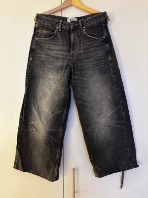 Svarta vida jeans från BDG Urban Outfitters storlek 26 - Säljer ett par svarta jeans från BDG Urban Outfitters med vid passform. Jeansen har klassisk femficksdesign, ljusa tvättade partier och broderad logga på ena bakfickan. Materialet är robust denim. OBS slitna detaljer vid bensluten. Benlängd - se bilder!