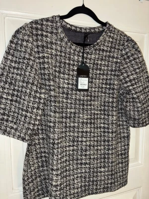 Rutig topp från Jyothi i offwhite - Snygg rutig topp från Jyothi i offwhite och svart. Modellen har rund halsringning och halvkort ärm. Tjockare vävt material som ger en cool struktur och trendig look. Perfekt att styla med jeans eller kjol för en chic vibe. Kommer även att sälja tillhörande kjol separat.