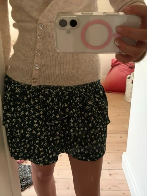 Grön blommig kortkjol med volang - Supersöt kortkjol i mörkgrönt med små vita blommor och volangkant. 