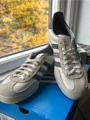 Adidas Gazelle Indoor White Preloved Ink - Adidas Gazelle Indoor sneakers i vit och grå mocka med blå ränder på sidorna. Skorna är inprincip slutsålda överallt och har galet högt andra hands värde. Jag har ett par i strl 42, och ett par i strl 41 1/3. Priset är såklart förhandlingsbart, och tveka inte på att höra av dig vid några frågor 