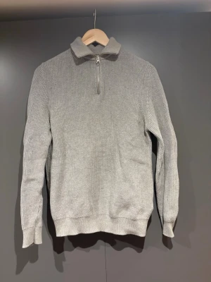 Grå stickad half zip-tröja från Zara - Säljer en grå stickad tröja från Zara med half zip och hög krage. Tröjan är ribbstickad och har långa ärmar, perfekt för kyliga dagar. Enkel och stilren design som funkar till det mesta.