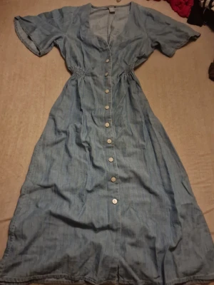 Blå jeansklänning från Lindex XS - Säljer en ljusblå jeansklänning från Lindex i storlek XS. Klänningen har korta ärmar, knappar hela vägen framtill och smock i midjan för en snygg passform. Perfekt till sommaren och enkel att styla med sneakers eller sandaler. Priset som står gäller, kan möjligtvis diskuteras 🫶