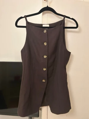 Brun topp H&M - Säljer en brun linnetopp från H&M med raka axelband och snygga knappar framtill. Toppen har en rak passform och är tillverkad i linneblandning som ger en skön känsla. Perfekt att styla med jeans eller kjol för en trendig look.