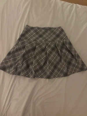 Grå rutig minikjol - Supersnygg minikjol i grått med rutigt mönster och breda veck. Kjolen har en klassisk A-linjeform och är perfekt för dig som gillar en preppy stil. Materialet känns mjukt och lätt, troligtvis bomull eller polyester. Passar perfekt till sneakers eller boots.