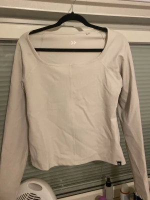 Vit långärmad topp från lager sporttröja  - Säljer en stilren vit långärmad topp från lager med bred, fyrkantig urringning. Toppen är ribbad och har en figurnära passform som sitter snyggt på kroppen. Perfekt att matcha med jeans eller kjol för en clean look.Den har bara en liten smink fläck men det löser jag!