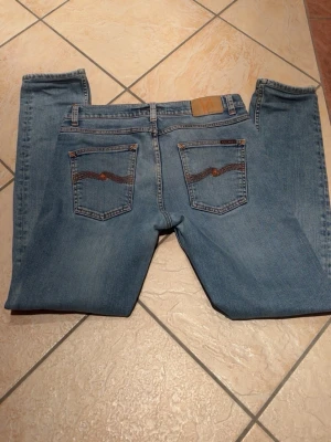 Nudie Jeans Lean Dean ljusblå 31/34 - Säljer ett par Nudie Jeans Lean Dean i ljusblå tvätt med klassisk orange brodering på bakfickorna. Modellen är Lean Dean och de är i storlek 31/34. Inga defekter utom lite på västra vaden men det läggs inte märke till när dom väl är på | Tveka inte med att höra av dig angående minsta lilla fundering🙏💛