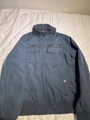 Tommy Hilfiger Multi Pocket Bomber Twilight Navy - Snygg mörkblå bomberjacka från Tommy Hilfiger med två bröstfickor med dragkedja och två sidofickor med knapp. Jackan har ribbade muddar och quiltat foder för extra värme. Sprillans ny och ej använd! 