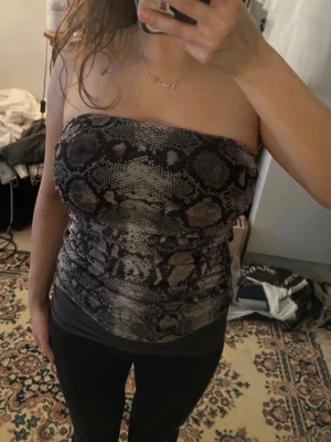 Ormmönstrad bandeau tubtopp från Zara - Säljer en snygg bandeau tubtopp från Zara med ormmönster i svart, grått och beige. Toppen är axelbandslös och har en tight passform med lätt rynkade detaljer på sidorna 💕