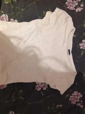 Vit t-shirt från Gina Tricot - En enkel och fräsch vit t-shirt från Gina Tricot i storlek S. Modellen är klassisk med rund hals och korta ärmar. Materialet känns mjukt och skönt, perfekt till jeans eller shorts. Stilren och lätt att matcha med andra plagg.