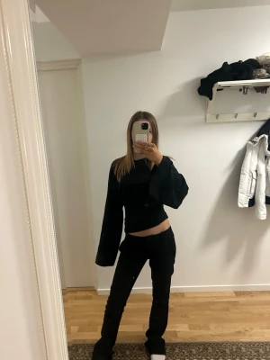 Svart långärmad topp med vida ärmar - Säljer en svart långärmad topp med riktigt vida ärmar och croppad passform. Toppen är enkel och stilren, perfekt att styla med jeans eller kjol. Materialet känns mjukt och stretchigt, troligen bomull eller polyester. Snygg och minimalistisk look.