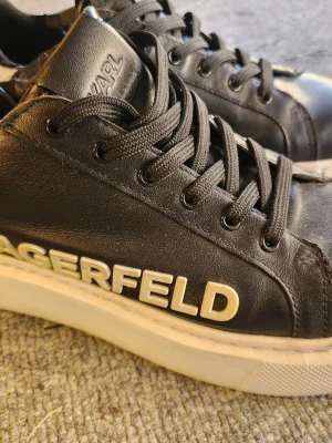 Karl Lagerfeld svarta sneakers - Svarta sneakers från Karl Lagerfeld med vit, grov sula och tydlig logga på sidan. Skorna har svart snörning och häl med präglad logga. Snygga och perfekta för dig som gillar streetstyle. Stl 37 men passar även en mindre 38.